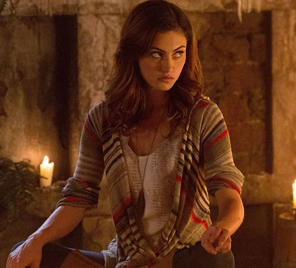 Young woman with long hair in a striped sweater sits in a dimly lit room with candles, looking to the side.