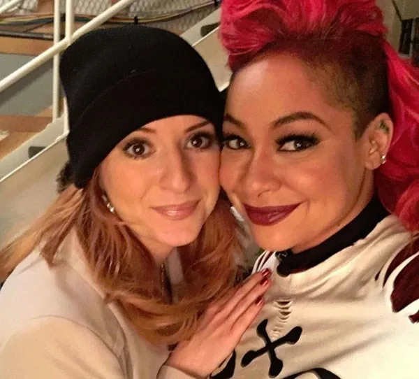 Two people posing together; one with red hair and a bold hairstyle, the other wearing a black beanie.