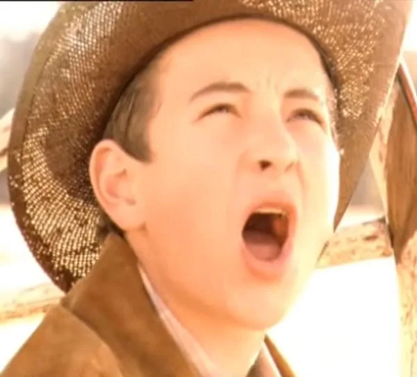 Young boy in a cowboy hat, mouth open, looking up with a bright light in the background.