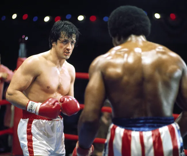 Two boxers in a ring wearing boxing gloves and trunks, facing each other during a match.