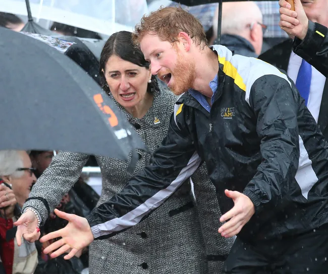 Two people under an umbrella, one in a coat and the other in a sports jacket, gesturing enthusiastically in the rain.