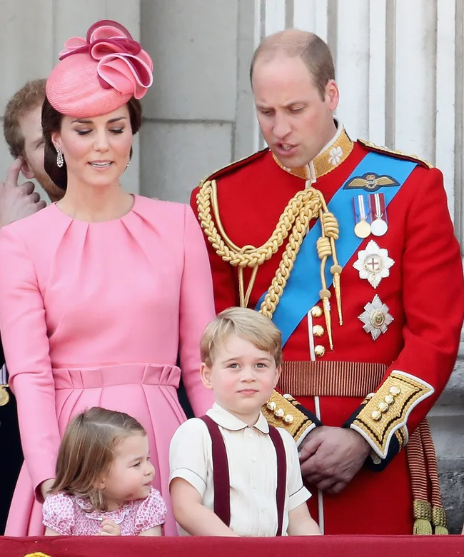 A family on a balcony during Trooping the Colour, with adults in formal attire and children watching.