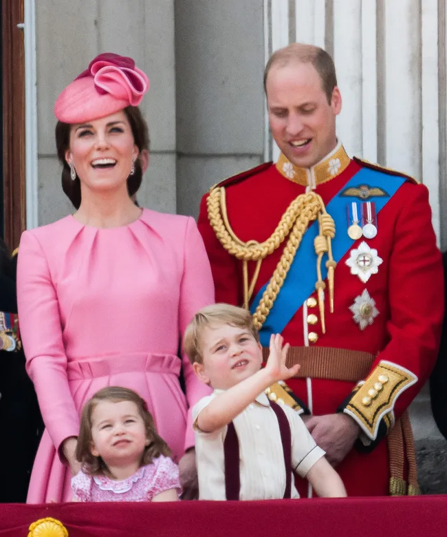 A family in formal attire stands smiling on a balcony during a public event.