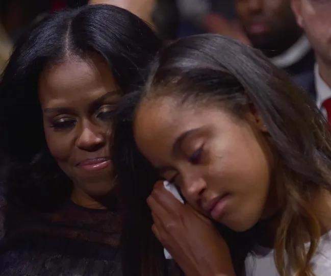 Two individuals sitting closely, one appears to be resting her head on a shoulder, with eyes closed, in a gentle, intimate moment.