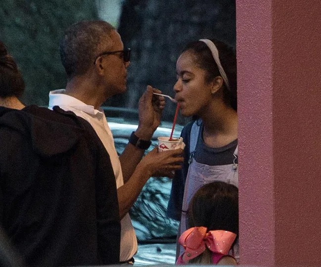 A man and woman share a frozen treat under dim lighting; the woman holds a straw.