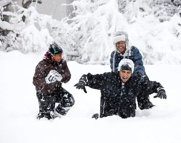 Three people enjoying a snowy day, laughing and bundled in winter clothing, surrounded by snow-covered trees.