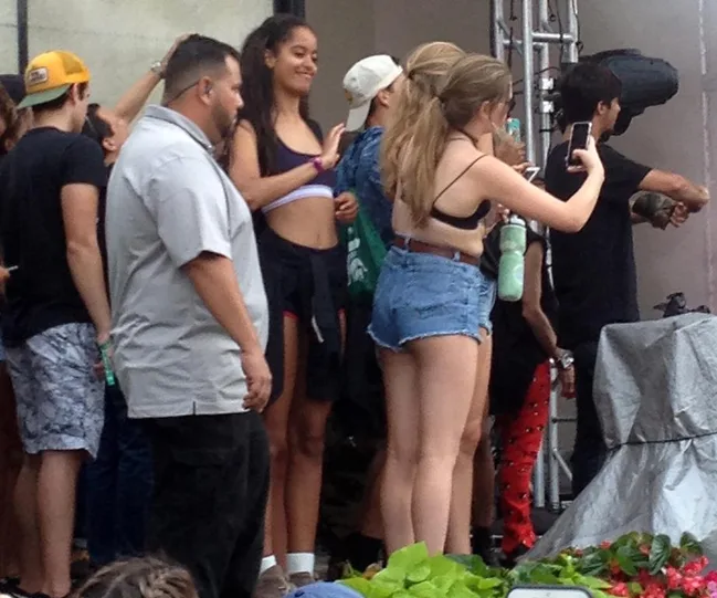 Group of young people at a concert, one taking a selfie, with a security guard in the foreground.