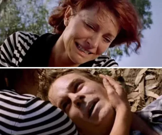 A distressed woman in stripes holds a man's face, depicting an emotional moment outdoors.