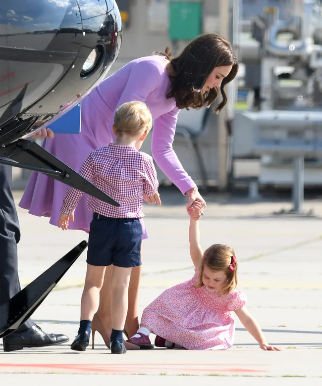 Mother helping young girl on tarmac while holding young boy's hand next to an aircraft.