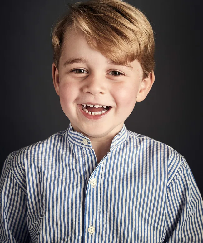 Smiling child with light hair wearing a blue and white striped shirt against a dark background.