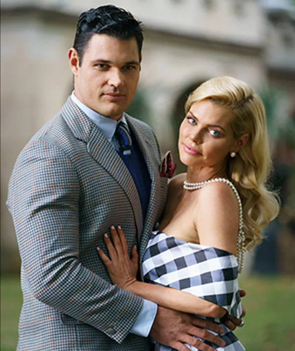 A man in a checkered suit and a woman in a plaid dress pose together outdoors, embracing.