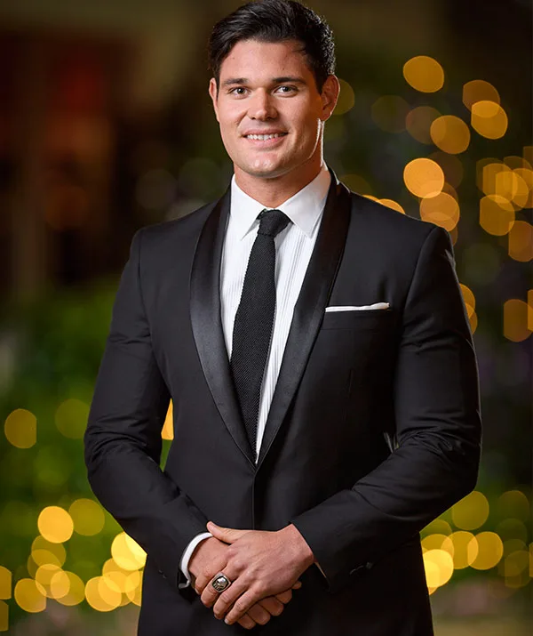 Person in a tuxedo with bokeh lights in the background, smiling.