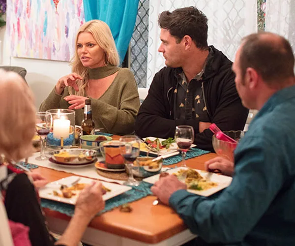 Group of people enjoying a meal together at a dining table, with food, drinks, and candles visible.