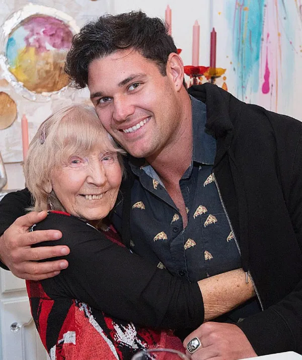 Older woman and younger man smiling and hugging, in a colorful setting with candles and wall art in the background.