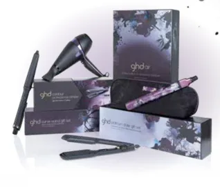 GHD hair styling set featuring a hair dryer, two stylers, packaging, and a black travel bag with a floral pattern.