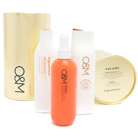 “Four O&M hair care bottles, including an orange spray, with gold packaging in the background.”