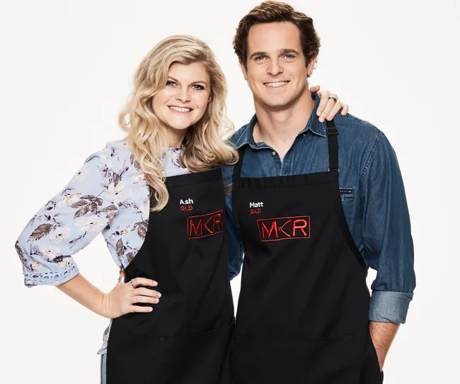 Young man and woman smiling, wearing "MKR" aprons labeled "Ash" and "Matt" from Queensland.