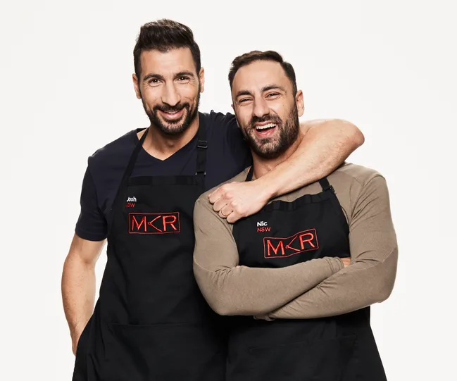 Two smiling men wearing "MKR" aprons, standing side by side against a white background.