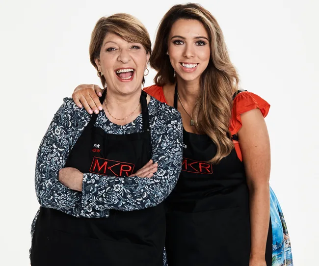 Two women wearing "MKR" aprons, smiling and posing, with one embracing the other.