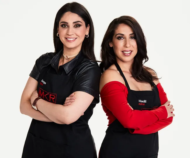 Two women wearing black aprons with arms crossed, smiling against a white background.