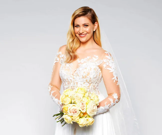 Bride in lace wedding gown holding yellow roses, smiling.