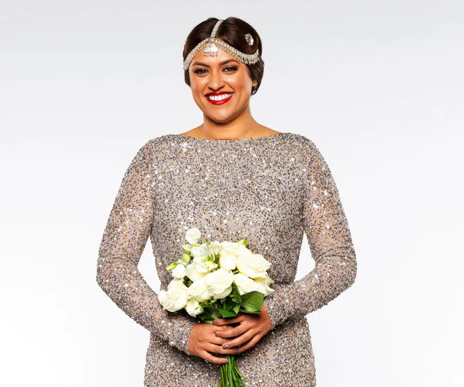 Person in sparkly dress holding bouquet, smiling at camera.