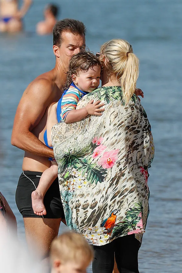 "A couple with a young child on a beach, wearing a colorful shawl, with the ocean in the background."
