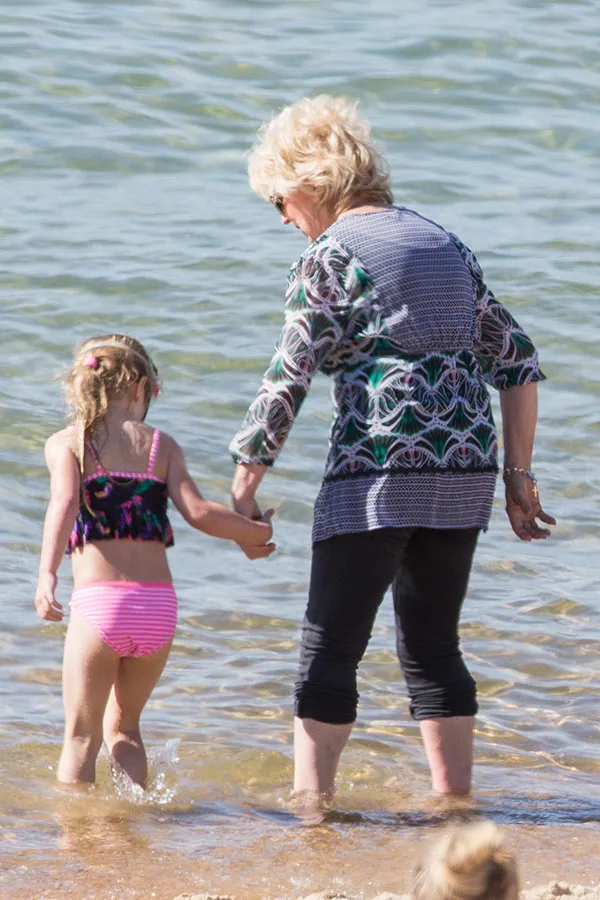A woman and a child holding hands, wading in the sea on a sunny day.