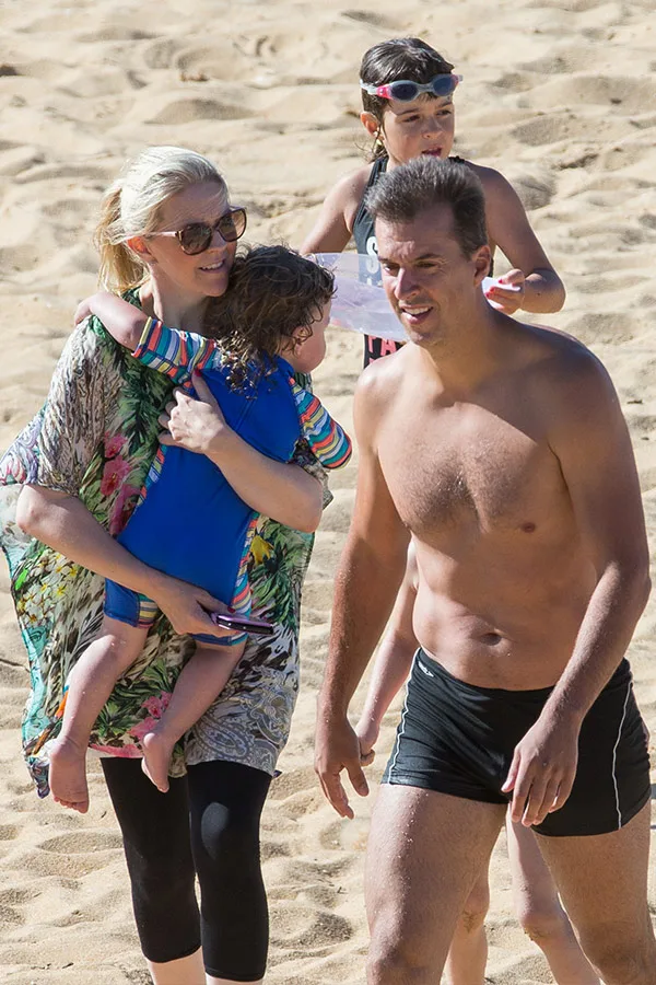 A family enjoying a day at the beach, with a woman holding a child and a man walking beside them.