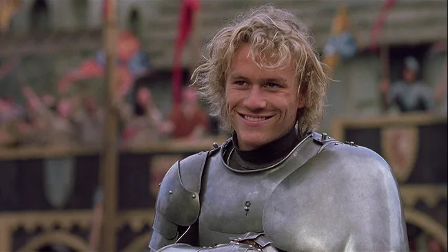 A knight in armor smiling at a medieval tournament scene.