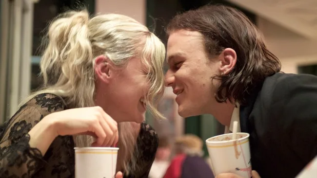 Young couple smiling and leaning close over milkshakes in a diner setting.