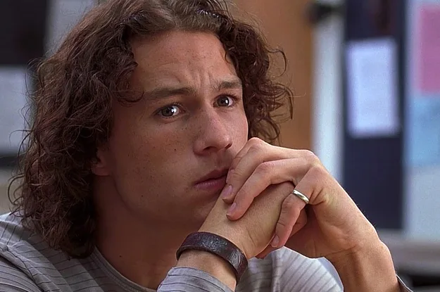 A person with long curly hair sits pensively with hands clasped under their chin, wearing a striped shirt.