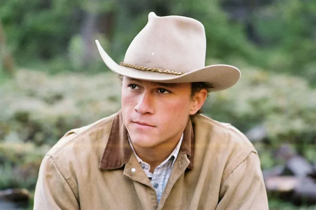 Cowboy in a beige jacket and hat gazing thoughtfully outdoors.