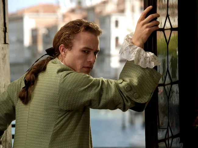 A person in period clothing leans on a door with a cityscape in the background.