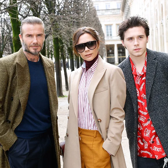 A family posing outdoors, dressed stylishly in coats; trees and a building in the background.