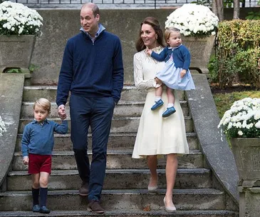 A family of four walks down outdoor steps, with two adults, a young boy holding hands, and a toddler being carried.