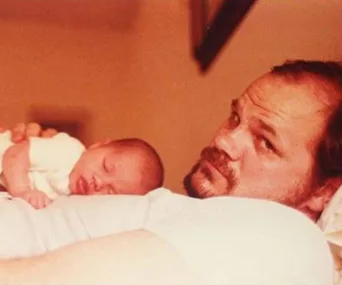 Father holding a sleeping newborn on his chest, both resting peacefully.