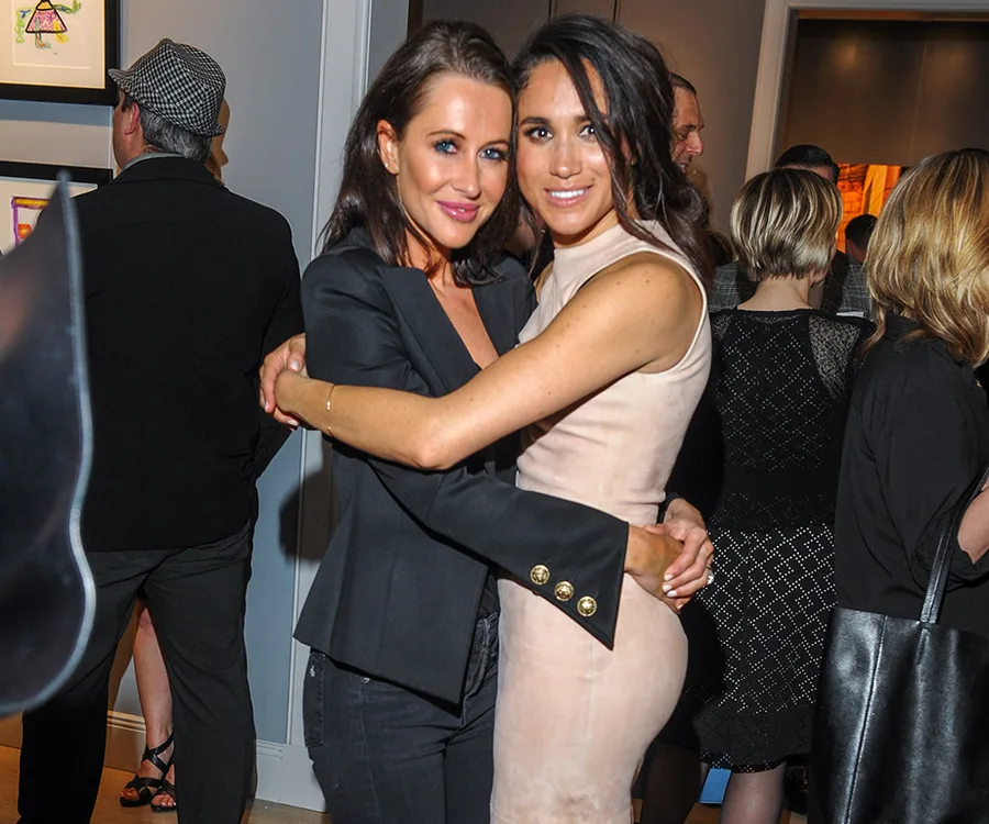 Two women embracing and smiling at a social event, surrounded by other people.