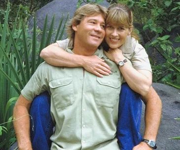 A couple embraces outdoors, surrounded by lush greenery.