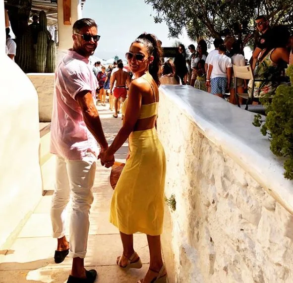 Couple holding hands on a sunny pathway with other tourists, smiling back at the camera.