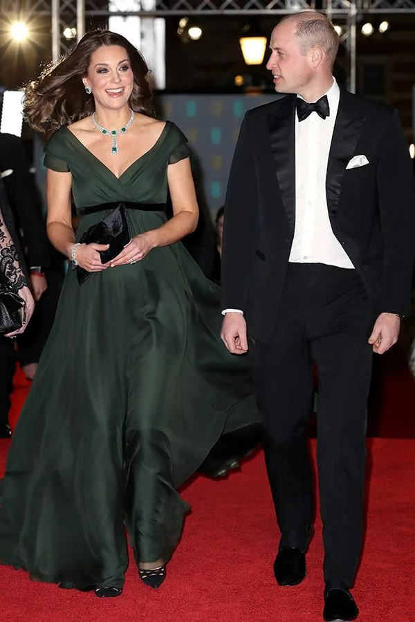 Two individuals walking on a red carpet; one in a green gown, the other in a tuxedo.