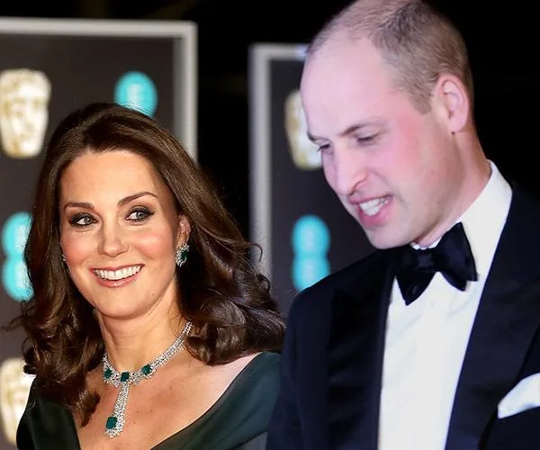 A man in a tuxedo and a woman in an elegant green dress and necklace smiling at an event.