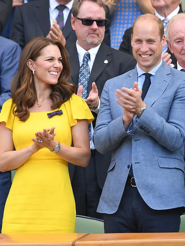 Couple clapping, woman in yellow dress, man in blue suit, surrounded by applauding crowd.