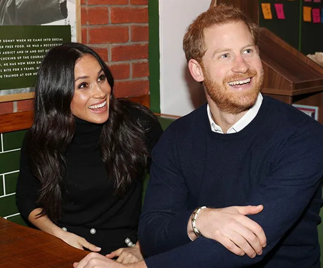 Two people smiling and sitting together at a wooden table in a casual setting with a brick wall in the background.