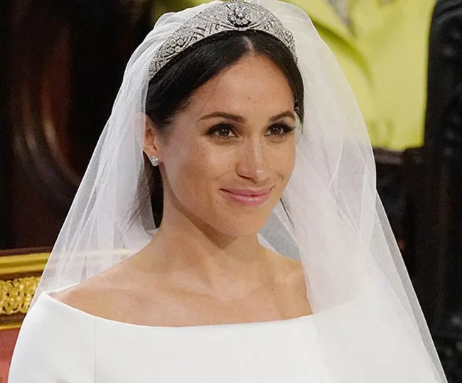 A woman in a white bridal gown and tiara smiles, wearing a veil during a formal ceremony.