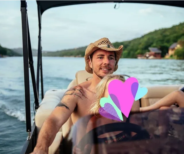 Man in cowboy hat steering a boat on a lake with blurred face of another person covered by graphic hearts.