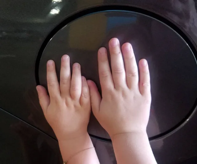 Two small hands placed on a car's round fuel cap door.
