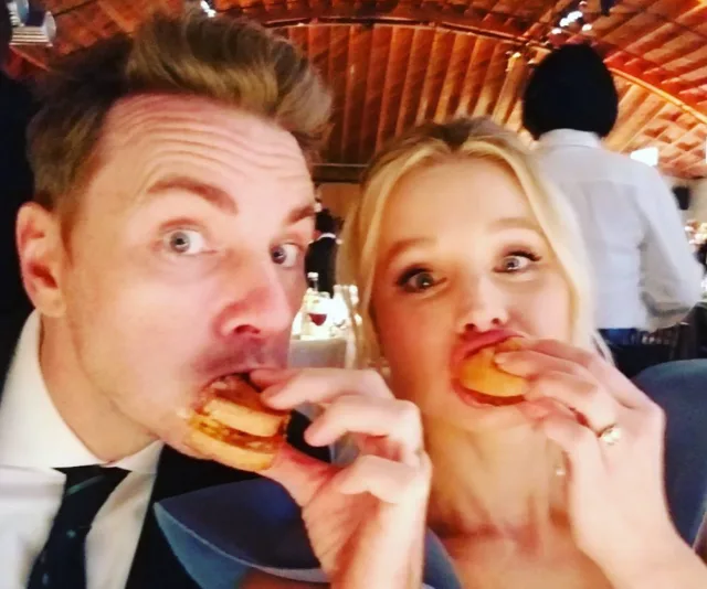 Two people enjoying mini burgers at a festive indoor event.