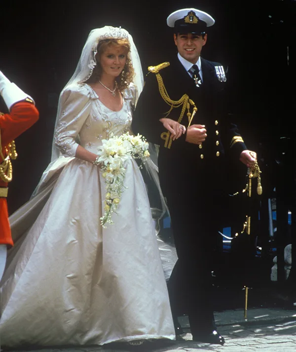 A bride in an elegant gown with a bouquet next to a groom in a navy uniform at a wedding ceremony.