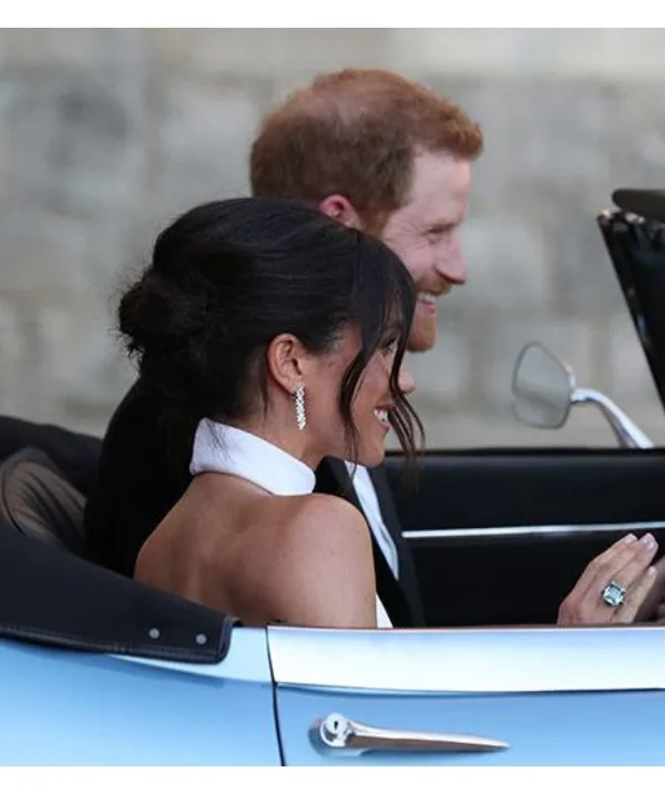 Couple in formal attire driving a car. Woman wears butterfly earrings and a large ring.